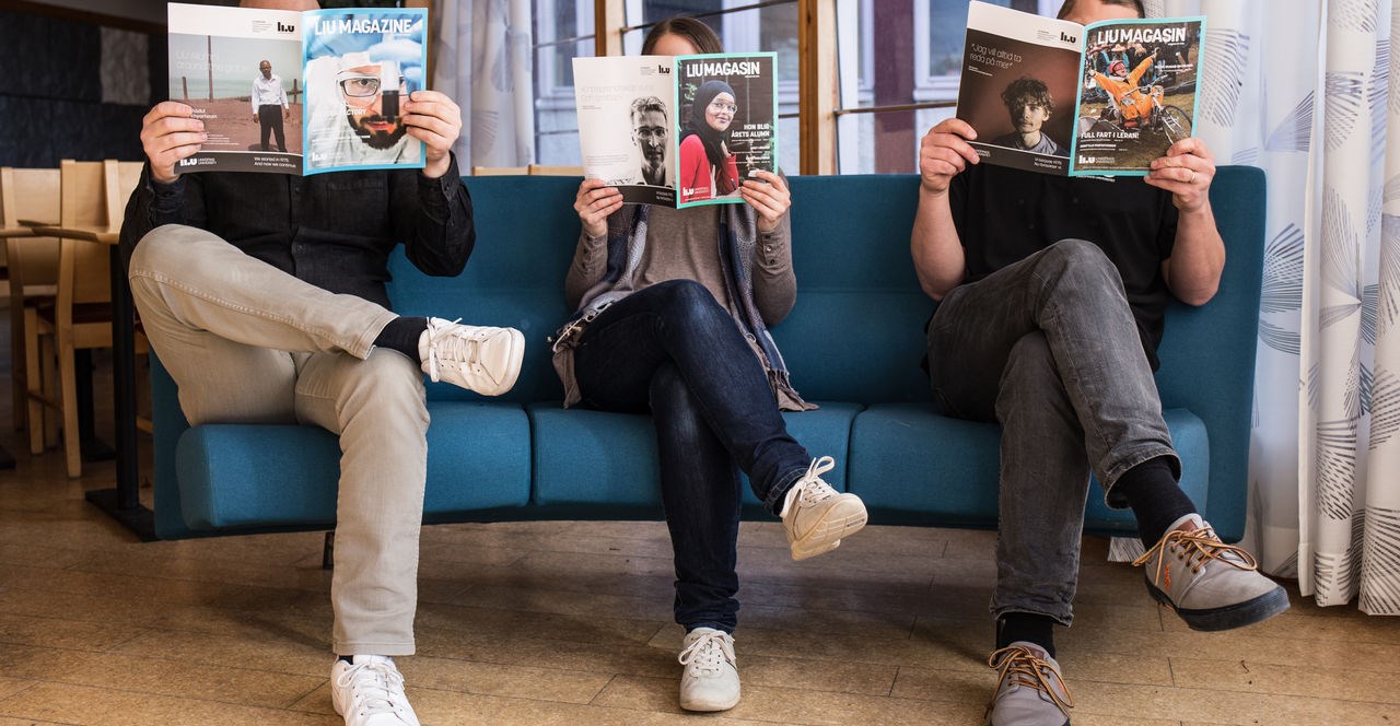 Three people sit in a sofa holding magazines so that they cover their faces