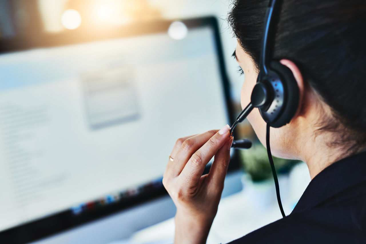 Woman talking in headset in front of computer.