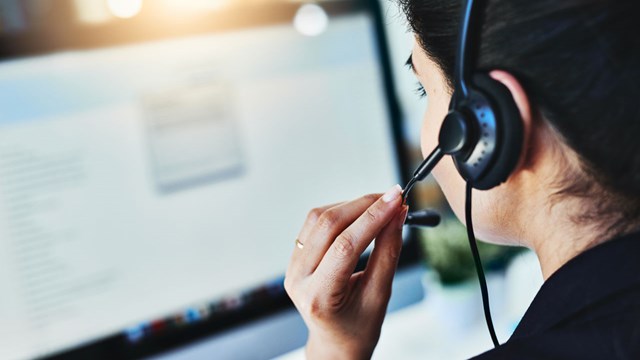 Woman talking in headset in front of computer.