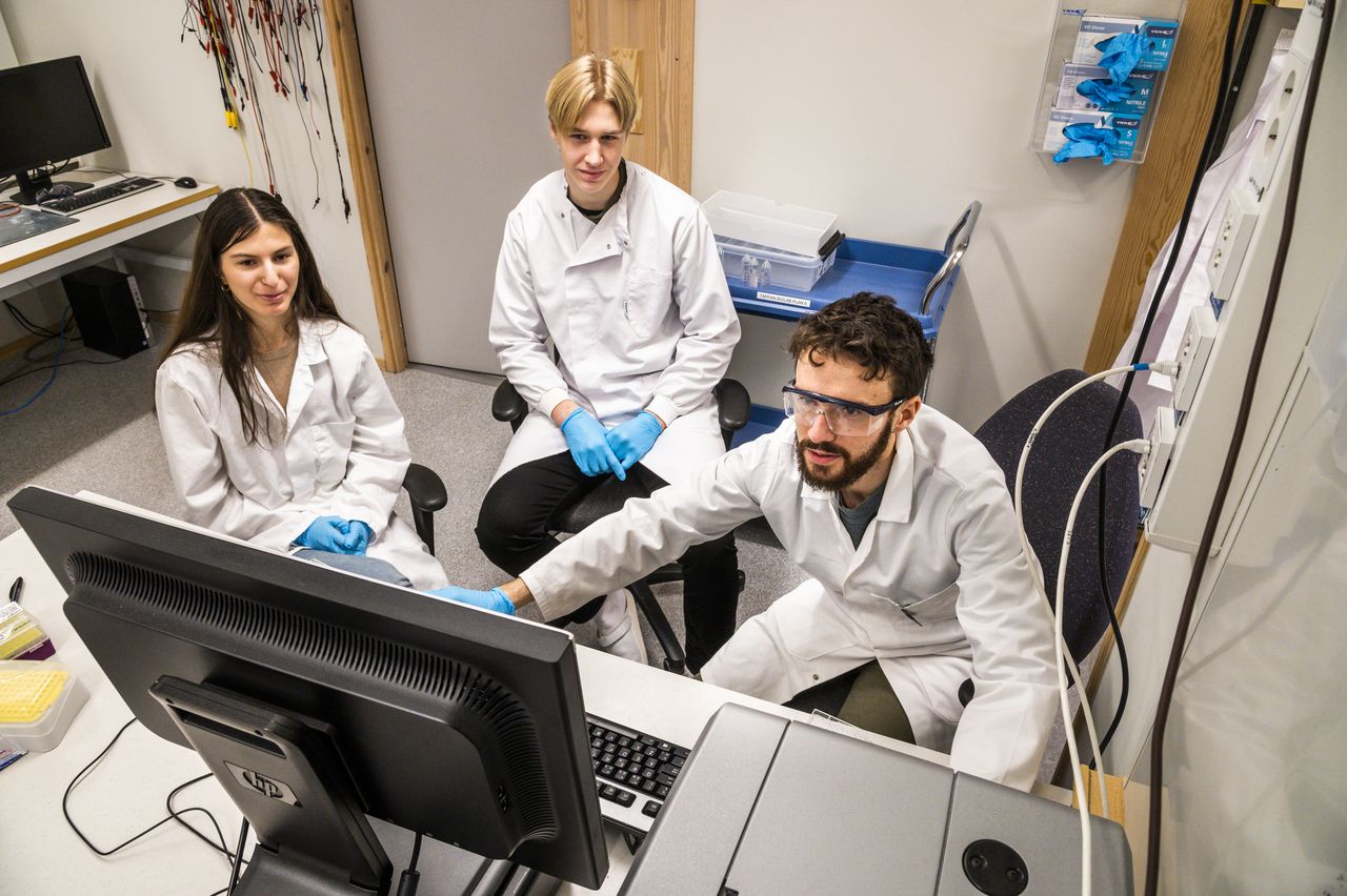Two highschool students looking at a computer screen where a researcher is showing something.