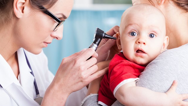 Young doctor examining baby boy with otoscope