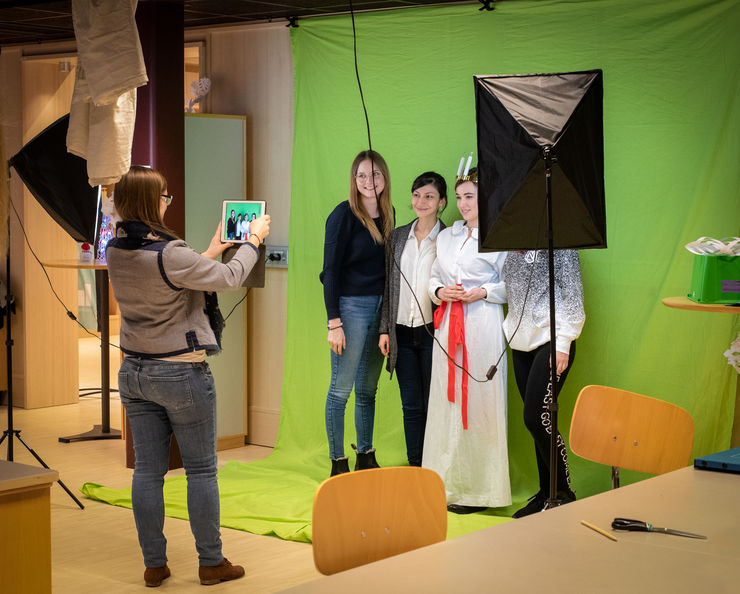 Four students being photographed against a green screen by a fifth student.