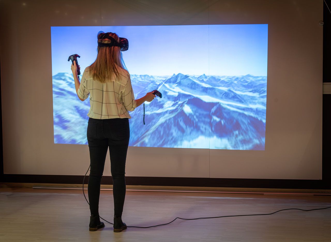 A female student wearing VR glasses in from of an image of a mountain landscape.