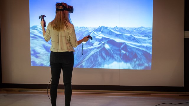 En student med VR-glasögon på sig mot en bild med ett bergslandskap.