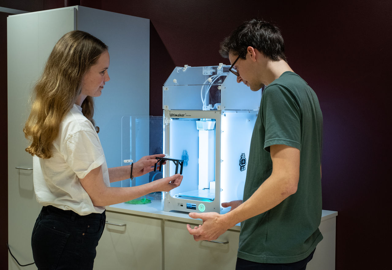 Two students standing by a 3D printer.