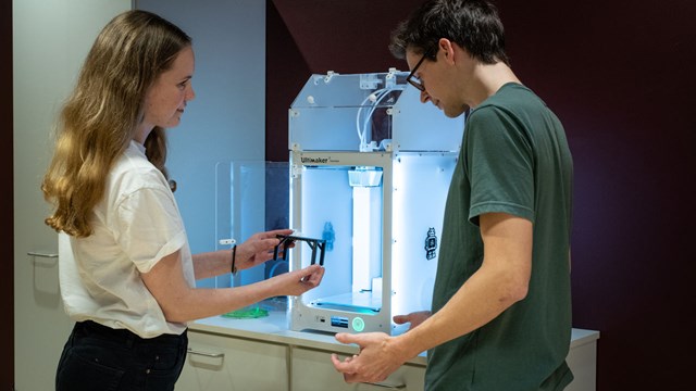 Two students standing by a 3D printer.