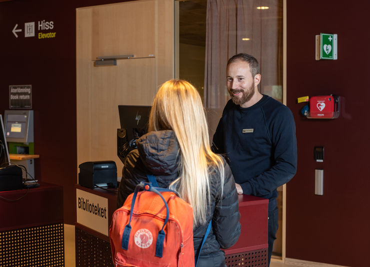 A librarian and a library visitor by a library enquiry desk.