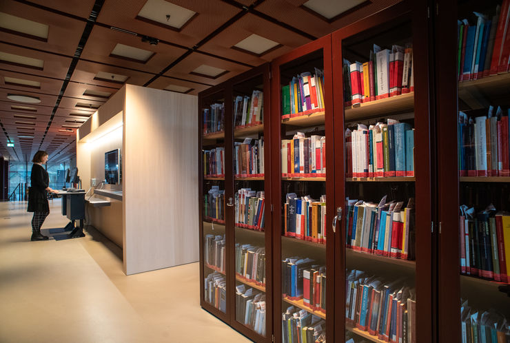 Book cabinets and a woman using a library self-check station.