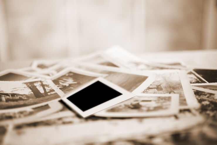 Many vintage, sepia-toned photographs from the 1940s lying in a large pile.  Old-fashioned memories from the past.  Antiques.  No people in this toned image and any people in the photos are unrecognizable.  Photos are of home lifestyles in the 1940s. Blank, Polaroid-style photo on top.