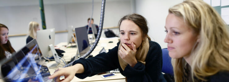 Två kvinnliga studenter sitter framför en dator och diskuterar.