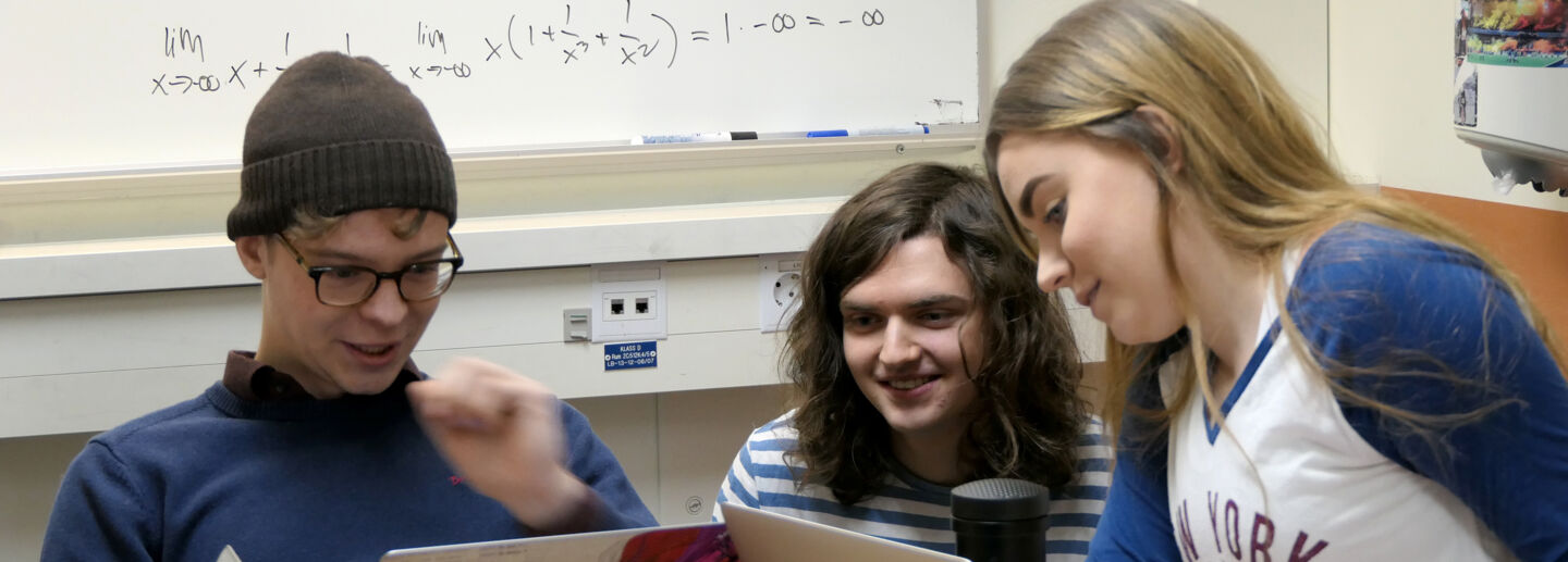 Tre studenter samarbetar bakom datorskärmar uttrycker nöjdhet 