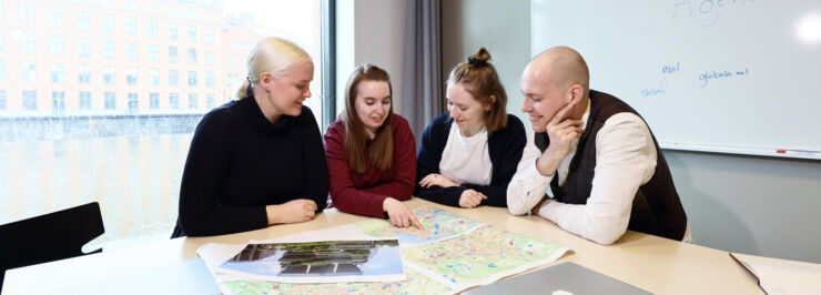 Tre kvinnliga och en manlig student sitter vid ett bord och studerar en karta. En kvinnlig student pekar på något på kartan.