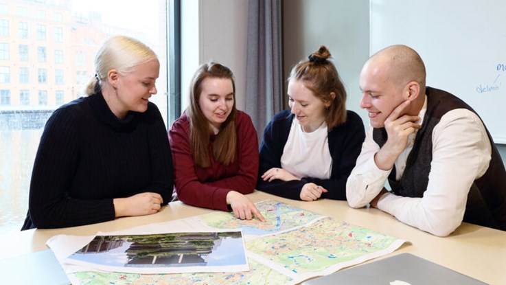 Tre kvinnliga och en manlig student sitter vid ett bord och studerar en karta. En kvinnlig student pekar på något på kartan.