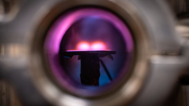 Through a window in the vacuum chamber, two purple spheres are observed.