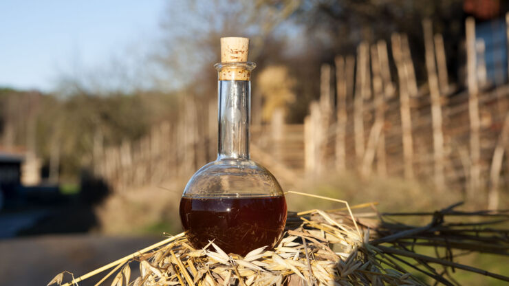 A capped bottle with red contents with nature in the background.