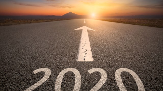 A road leading to a sunset. 2020 is written on the road with white paint, above it an arrow is pointing in the direction of the horizon.