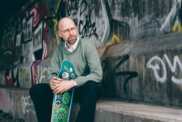 A man sits with a skateboard in his hand.