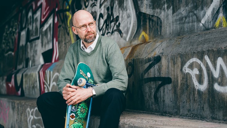 A man sits with a skateboard in his hand.