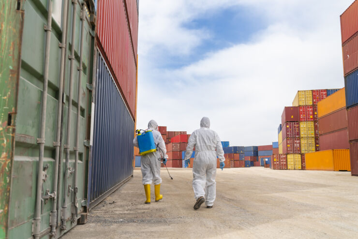 People wearing protective suits spray disinfectant chemicals on the cargo container to prevent the spreading of the coronavirus.