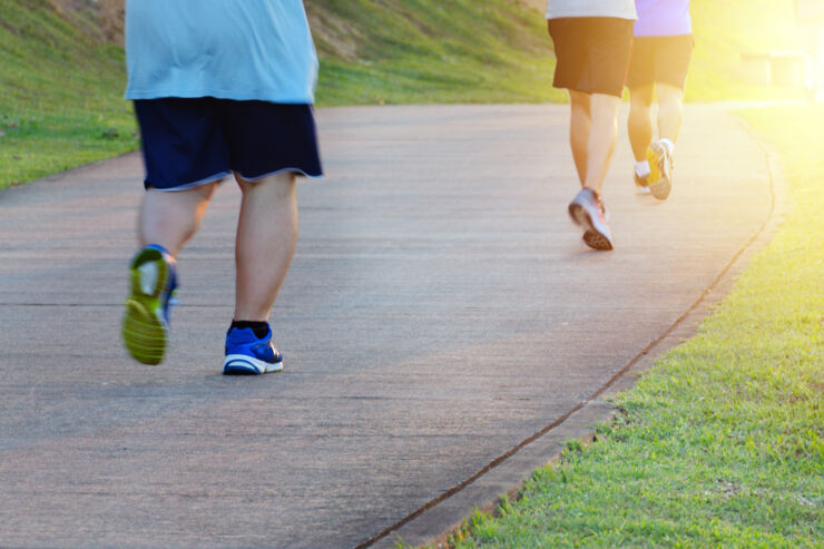 Fat man jogging, catching up with thin men. Low angle view of runners running in park. Blurred feet motion group of runners, Fitness and healthy lifestyle, outdoor sports activity. Copy space.