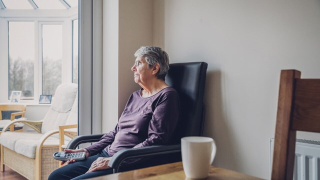 Senior woman sitting alone in her kitchen. She is looking out into her conservatory while holding a home telephone in her hand. Serious expression