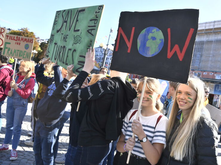 Två blonda flickor håller en skylt på en klimatdemonstration. I bakgrunden syns fler människor och skyltar.