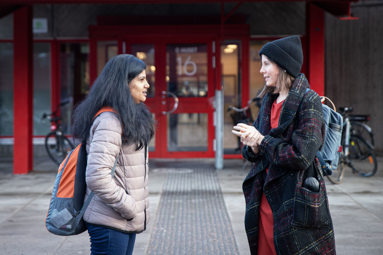 Två kvinnliga studenter som samtalar utanför en entré till en universitetsbyggnad.