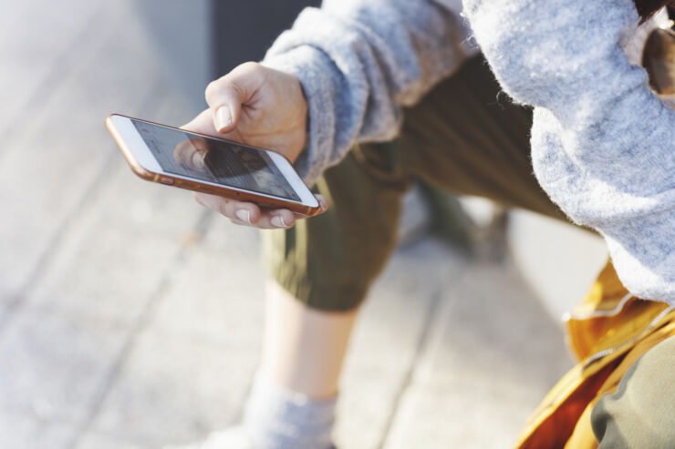 En person sitter ner utomhus och håller en mobiltelefon i handen.