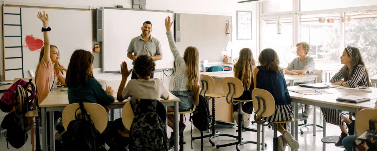 Elever räcker upp handen när lärare håller i en lektion.