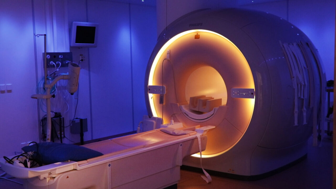 Photo of a MR camera. There is a blue light on the walls from the machine and there is a red, soft light coming from the middle of the machine.