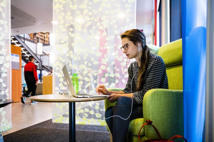 A female student sitting in an armchair and using a laptop.