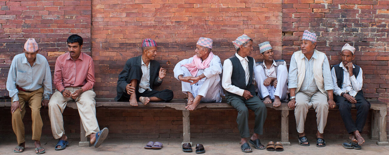 Line of men sitting and talking in front of wall.