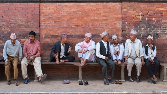 Men sitting in front of wall talking.