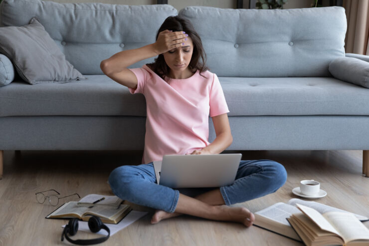 Woman sits on the floor with a laptop, a hand on her forehead