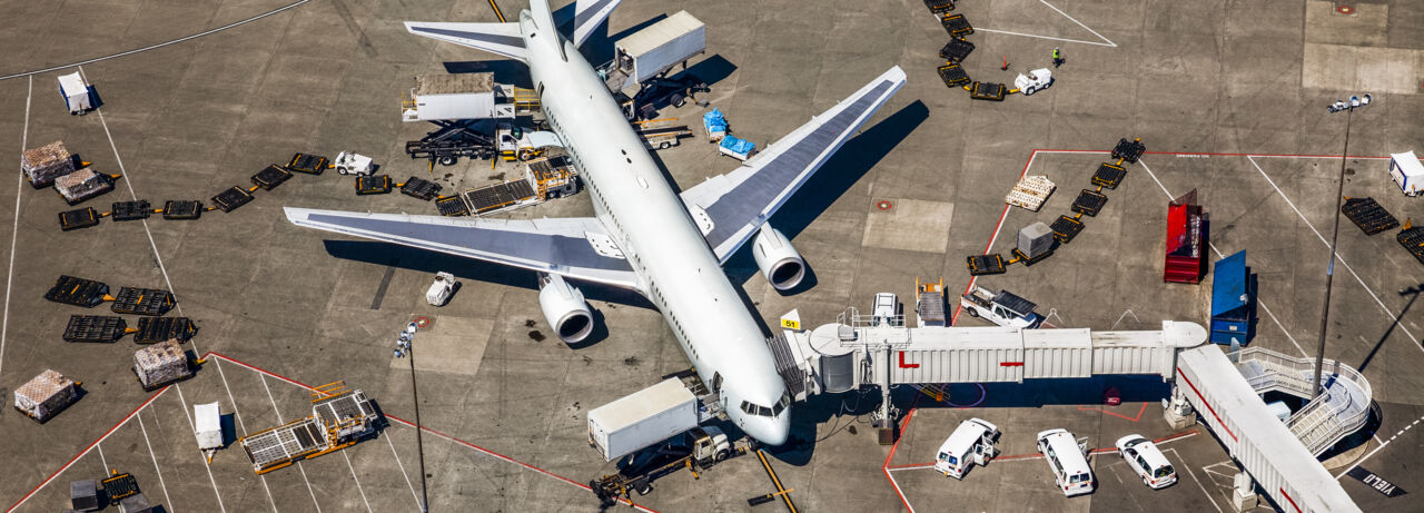 Flygplan vid gate på flygplats. Fordon och maskiner förbereder planet inför flygning.