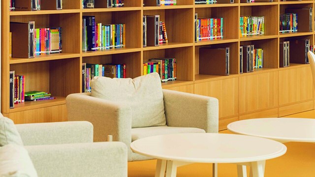 Två stolar med bord vid några bokhyllor i ett bibliotek. 