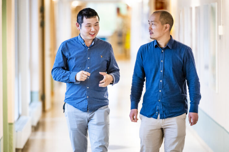 Two male scientists walks and talks in a hallway.