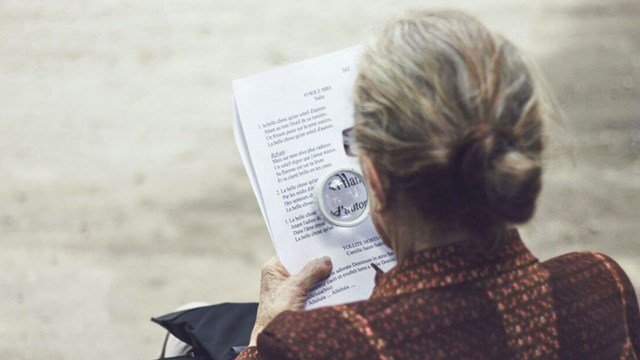 Kvinna som använder ett förstoringsglas för att läsa.