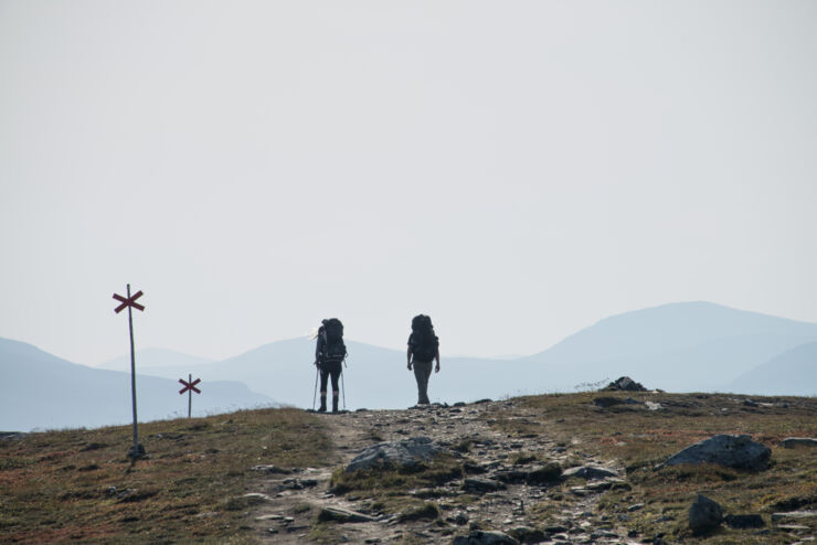  Two people are hiking along a trail on a mountain. Both have large backpacks on and they are walking away from the camera.