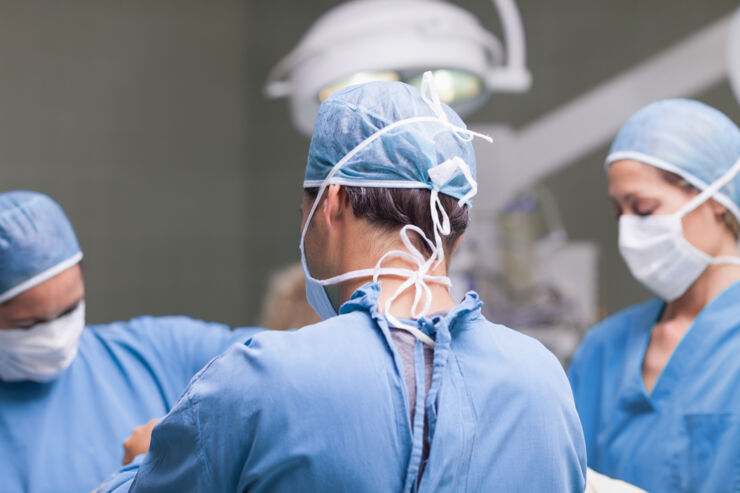  Close up of three doctors dressed in surgical clothes. One stands with his back to the camera.