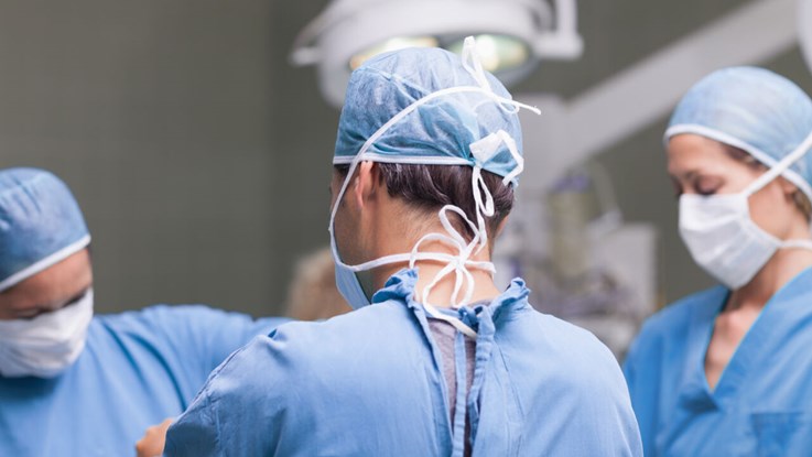  Close up of three doctors dressed in surgical clothes. One stands with his back to the camera.