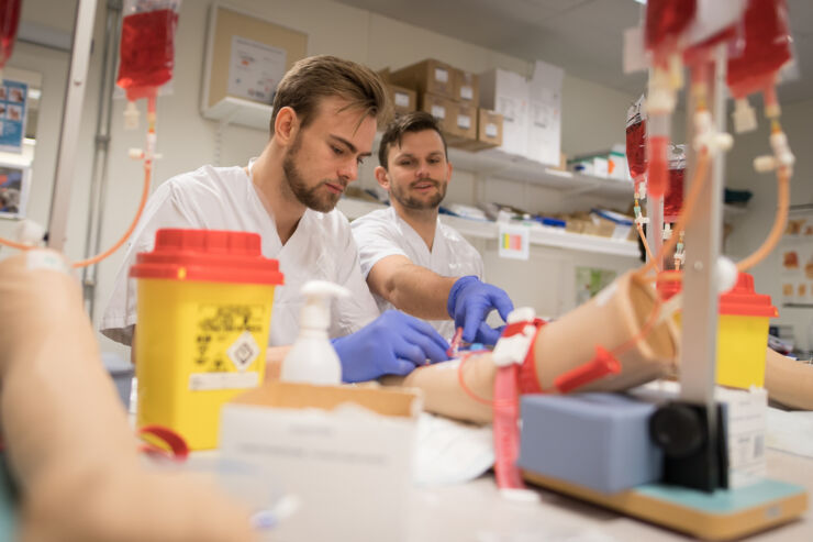 Two men dressed in white and wearing blue gloves, in front of a table with laboratory equipment.