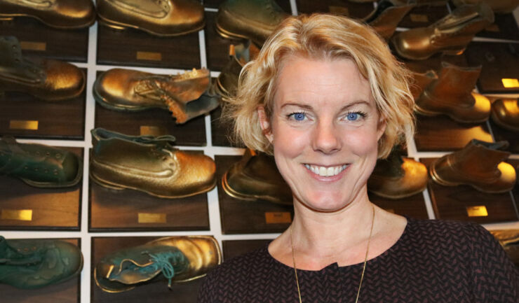 Woman by a wall full of golden-coloured shoes. 