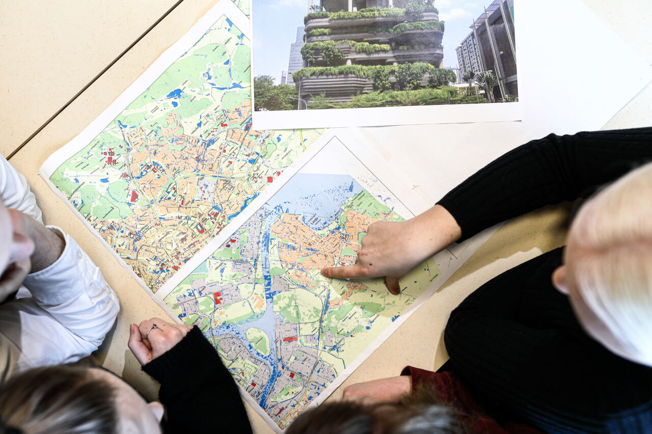 Coles-up of map, seen from above. One person, also seen from above is pointing at the map