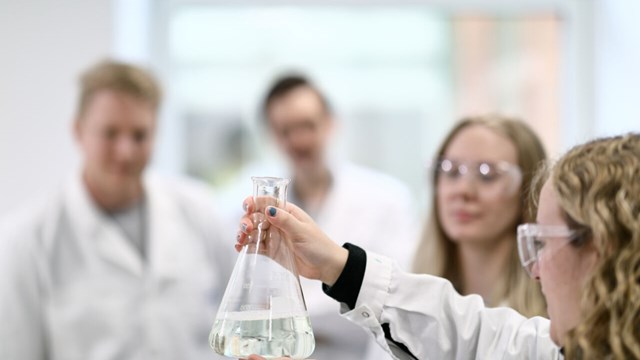 Studenter i labbmiljö. en student håller upp ett kärl i glas