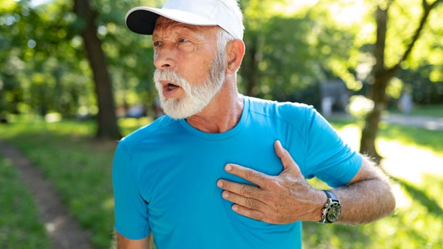 Äldre man lägger handen över hjärtat på joggingtur.