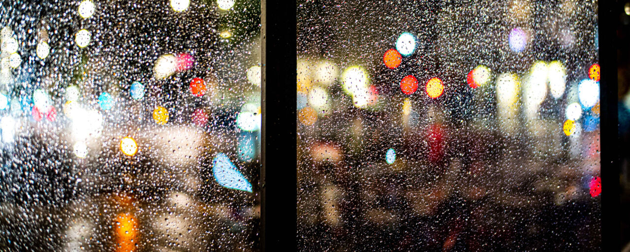 Photo on a rainy lit up street, taken through a window.