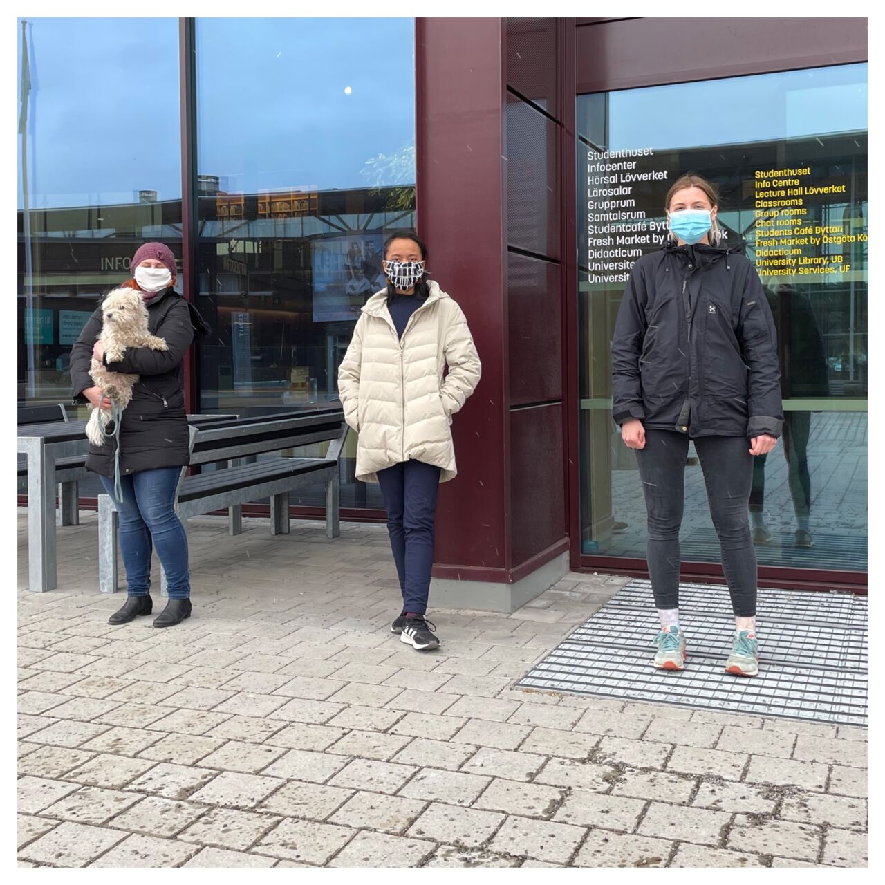 Three people are standing outside the building with face masks.