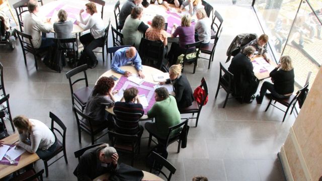Människor sitter runt bord och diskuterar.