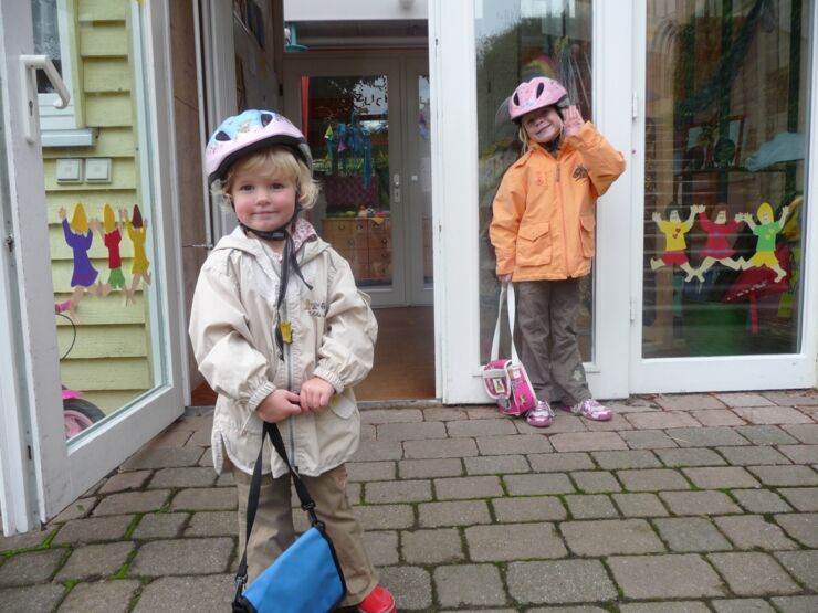 Två glada barn med cykelhjälmar står utanför förskola